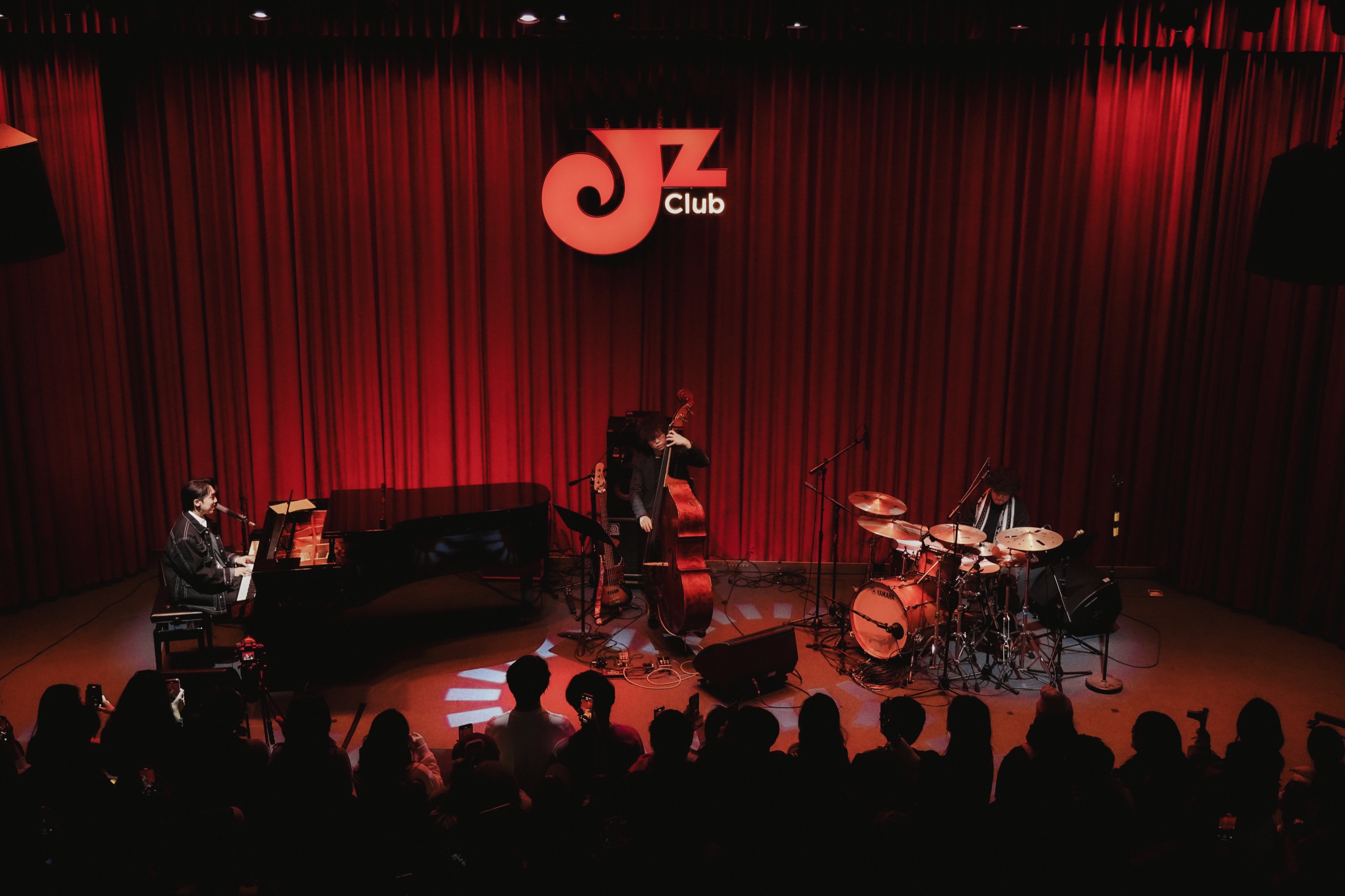 A pianist, bassist, and drummer performing before a live audience