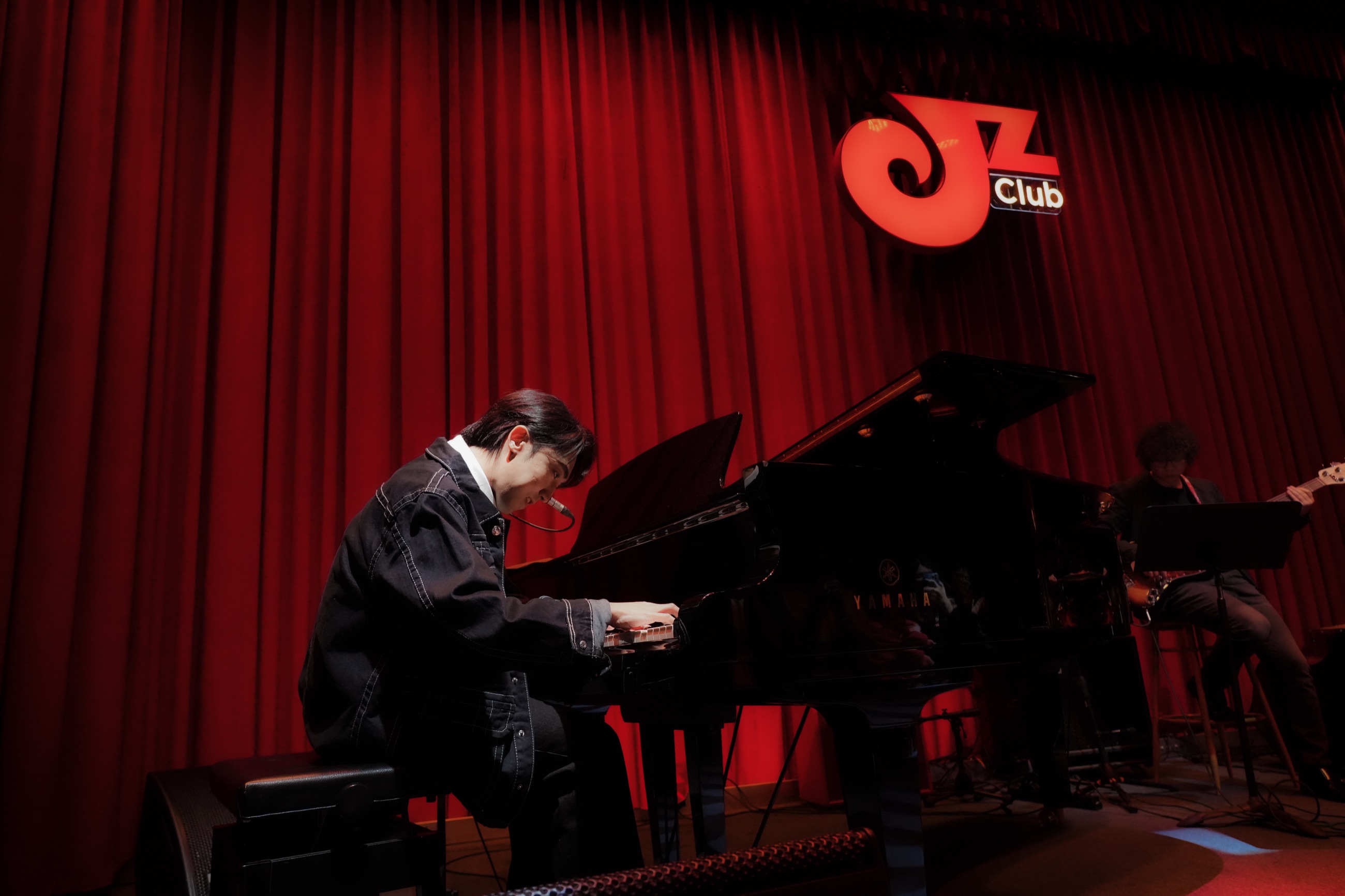 A wide view of the pianist at a grand piano on a red-curtained stage