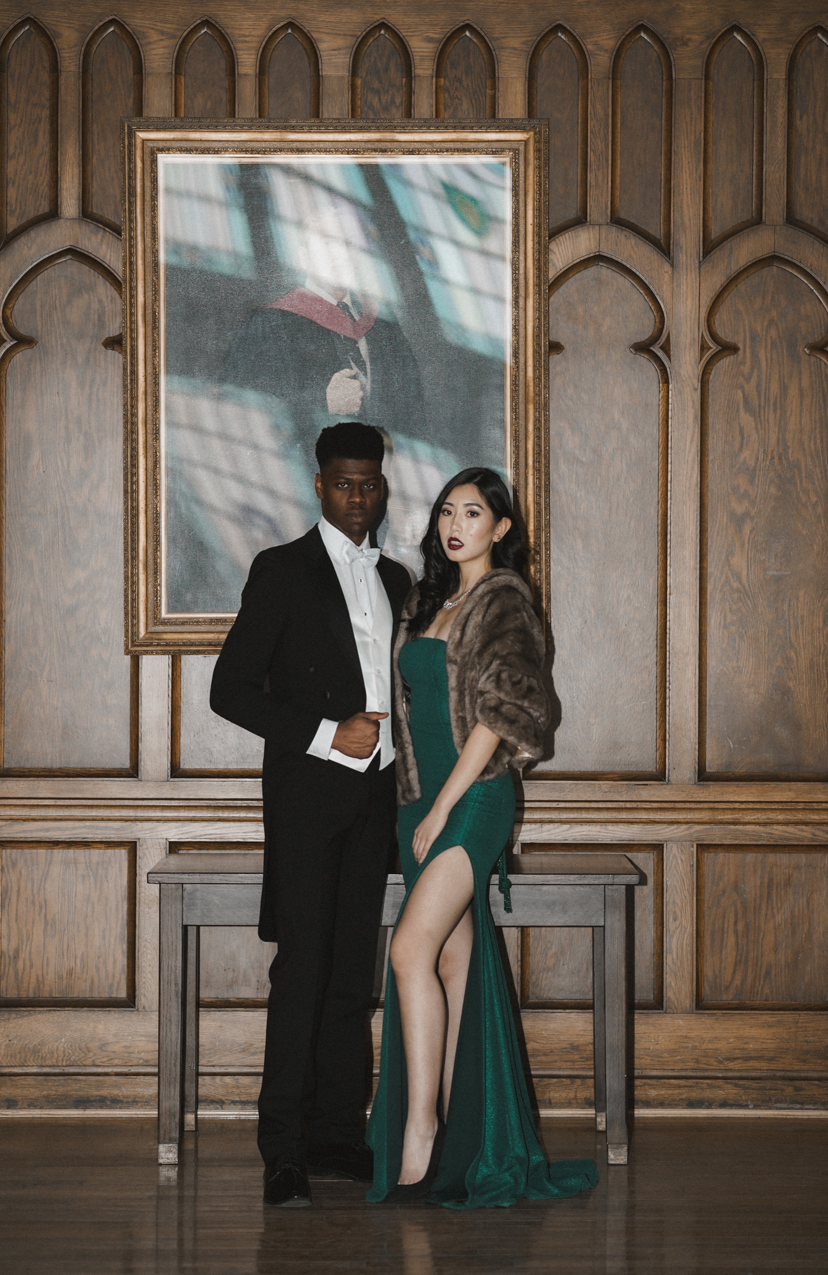 A formal couple posing beneath a framed portrait and carved woodwork