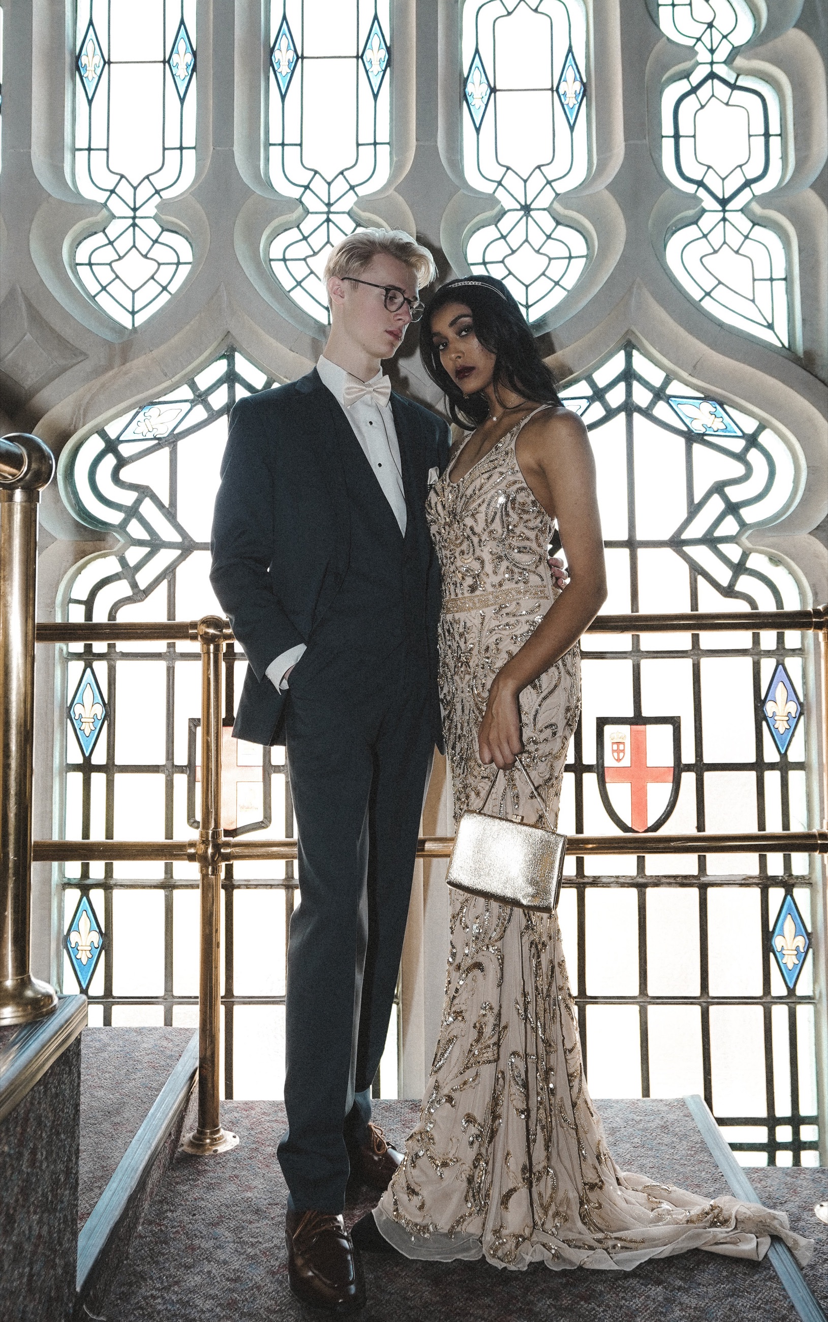 A formally dressed couple posing before ornate stained-glass windows