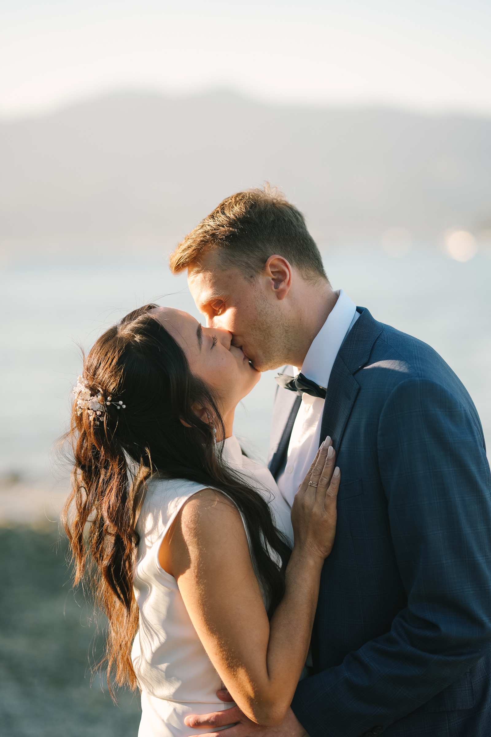 Newlyweds kissing in golden light beside the water