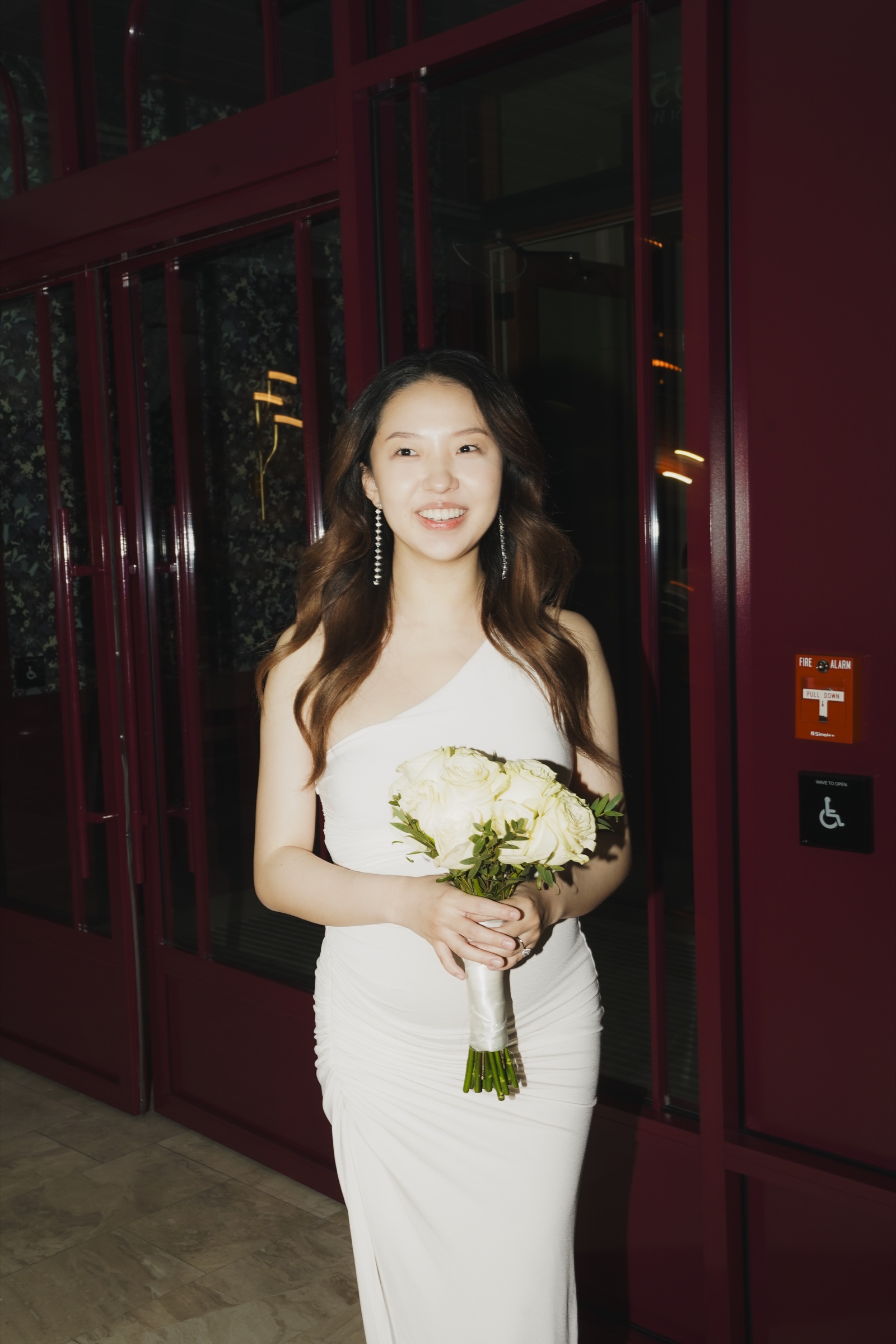 A bride holding white roses before burgundy doors