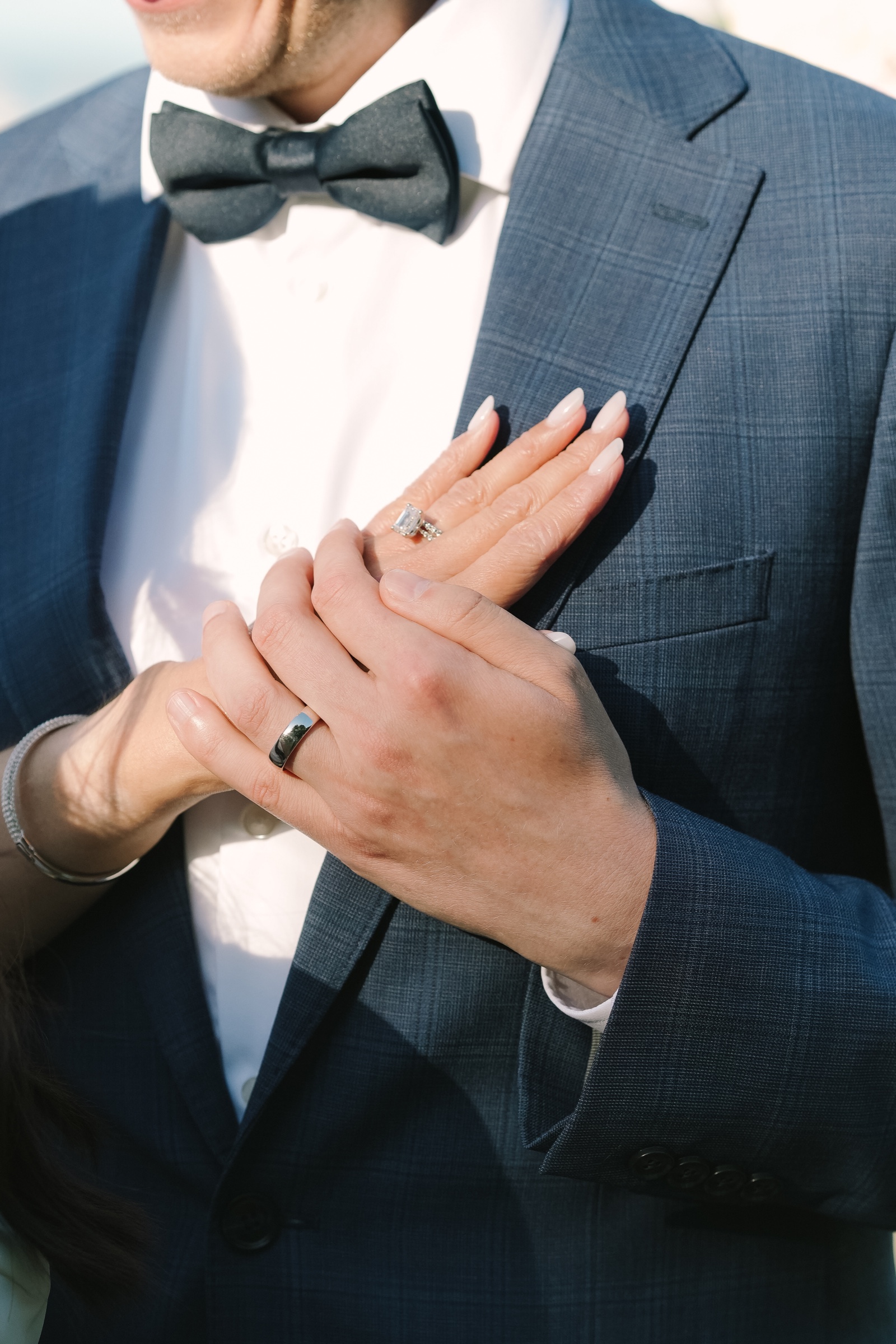 Newlyweds showing their wedding rings against a blue suit