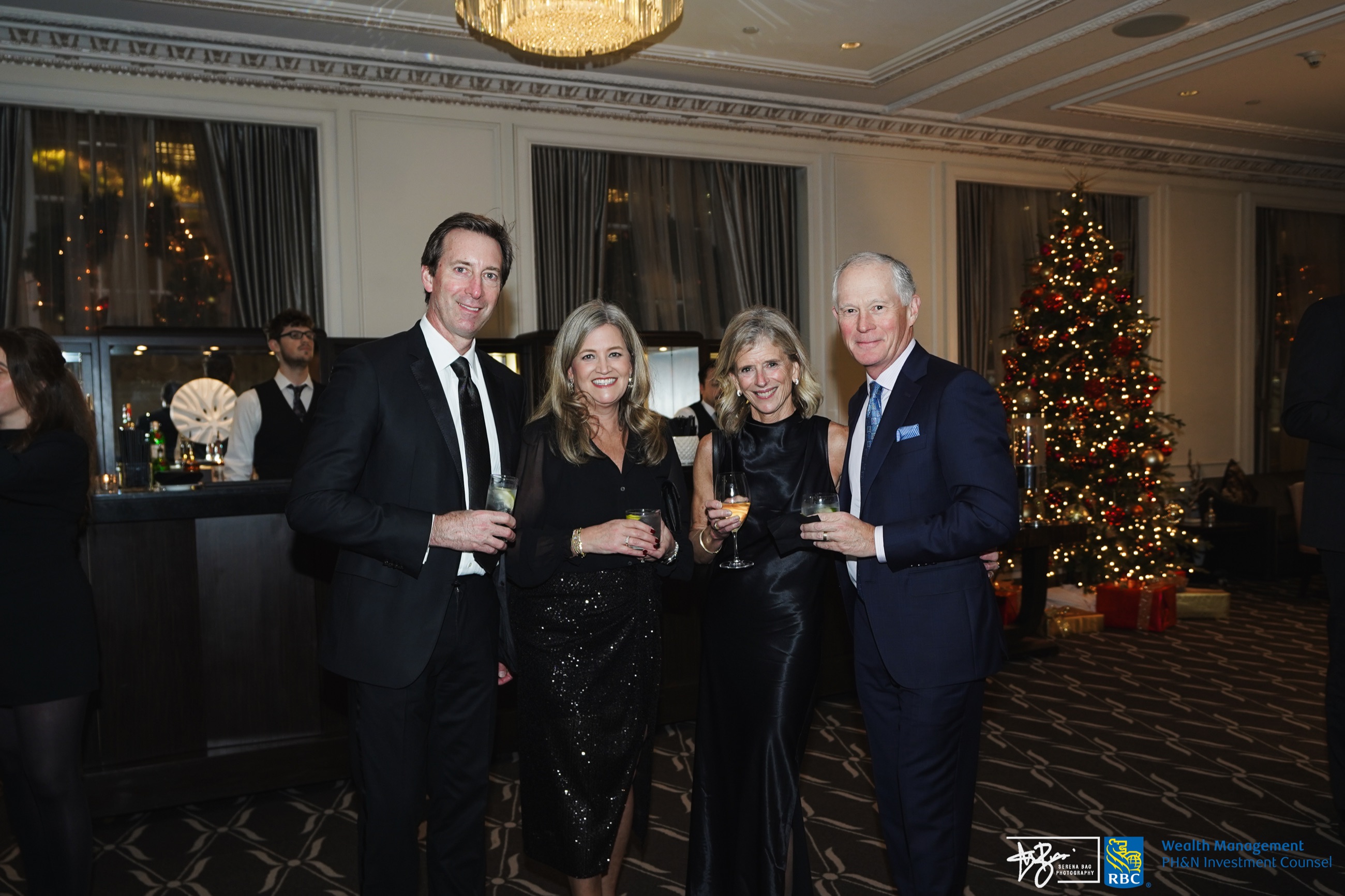 Four guests posing together beside a decorated Christmas tree