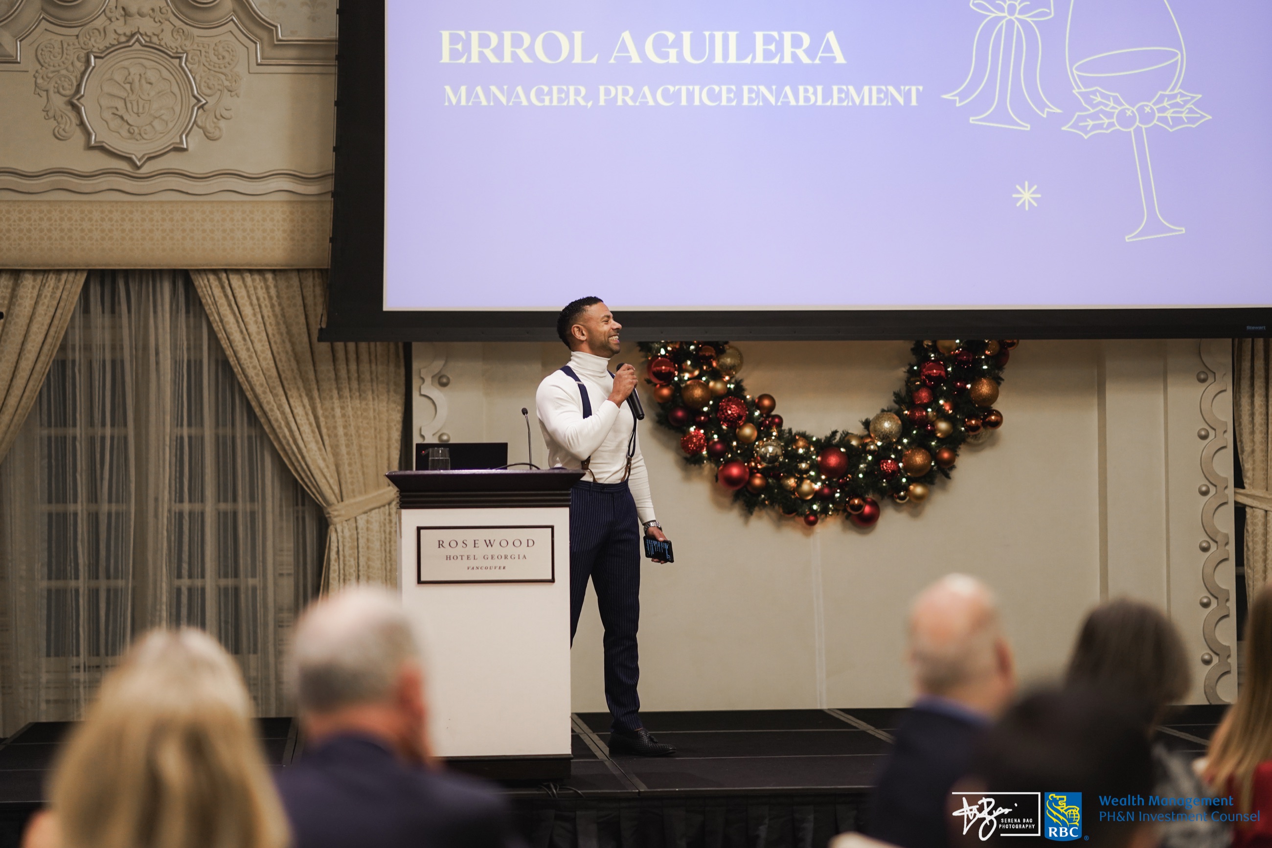 A host presenting from the stage beneath Christmas decorations